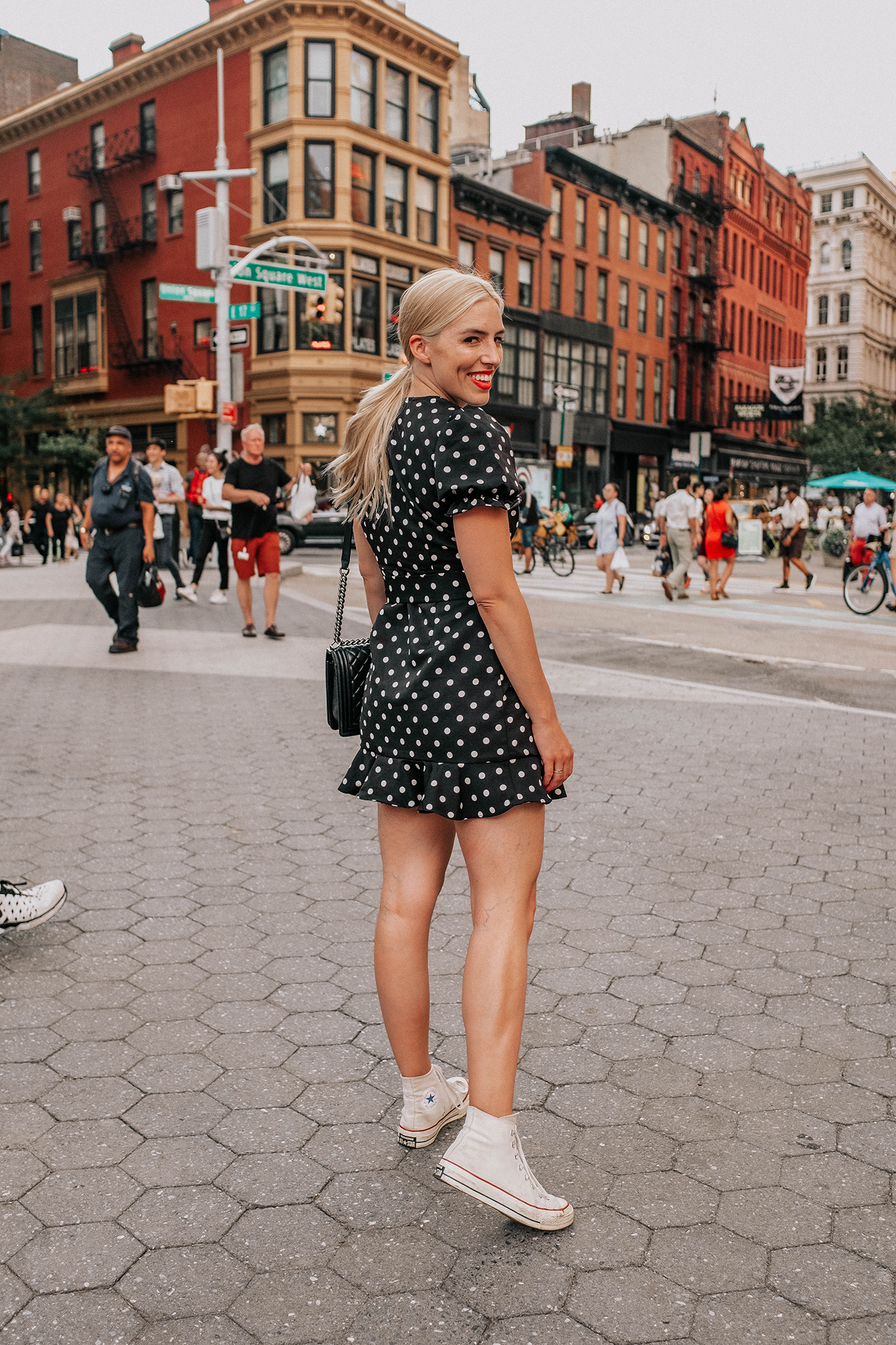 woman in the streets, smiling and wearing polka dot dress and white sneakers