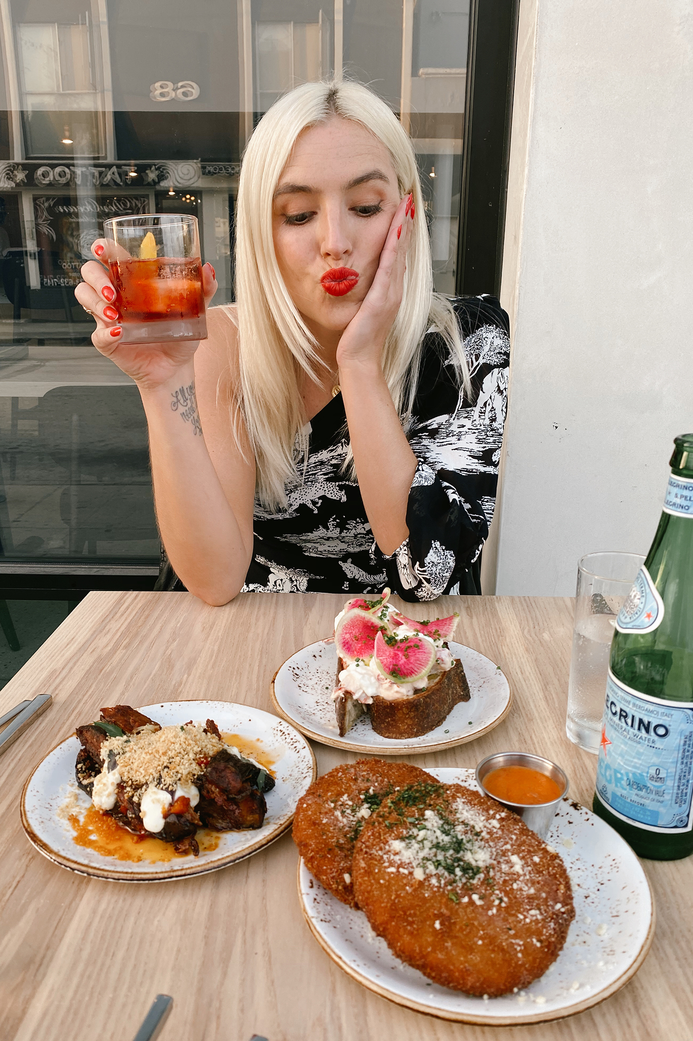 woman holding a drink and resting her elbows in a table with food in one of the best new restaurants in LA